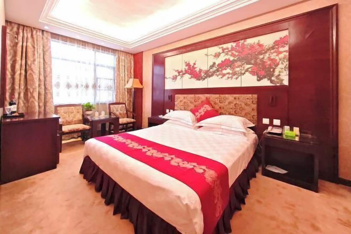 A hotel room with a large bed, a desk, a chair, a nightstand, and a painting on the wall.