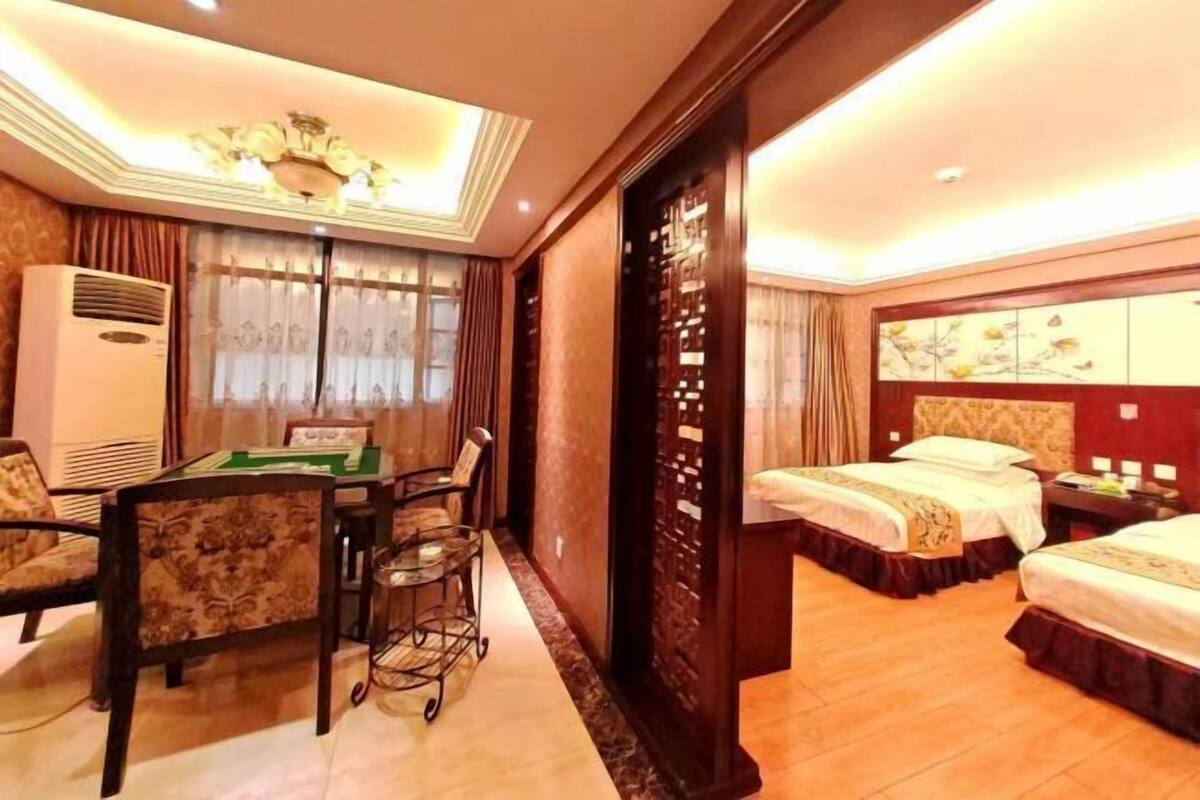 A hotel room with a desk, chairs, a bed, a wardrobe, and a ceiling light fixture.