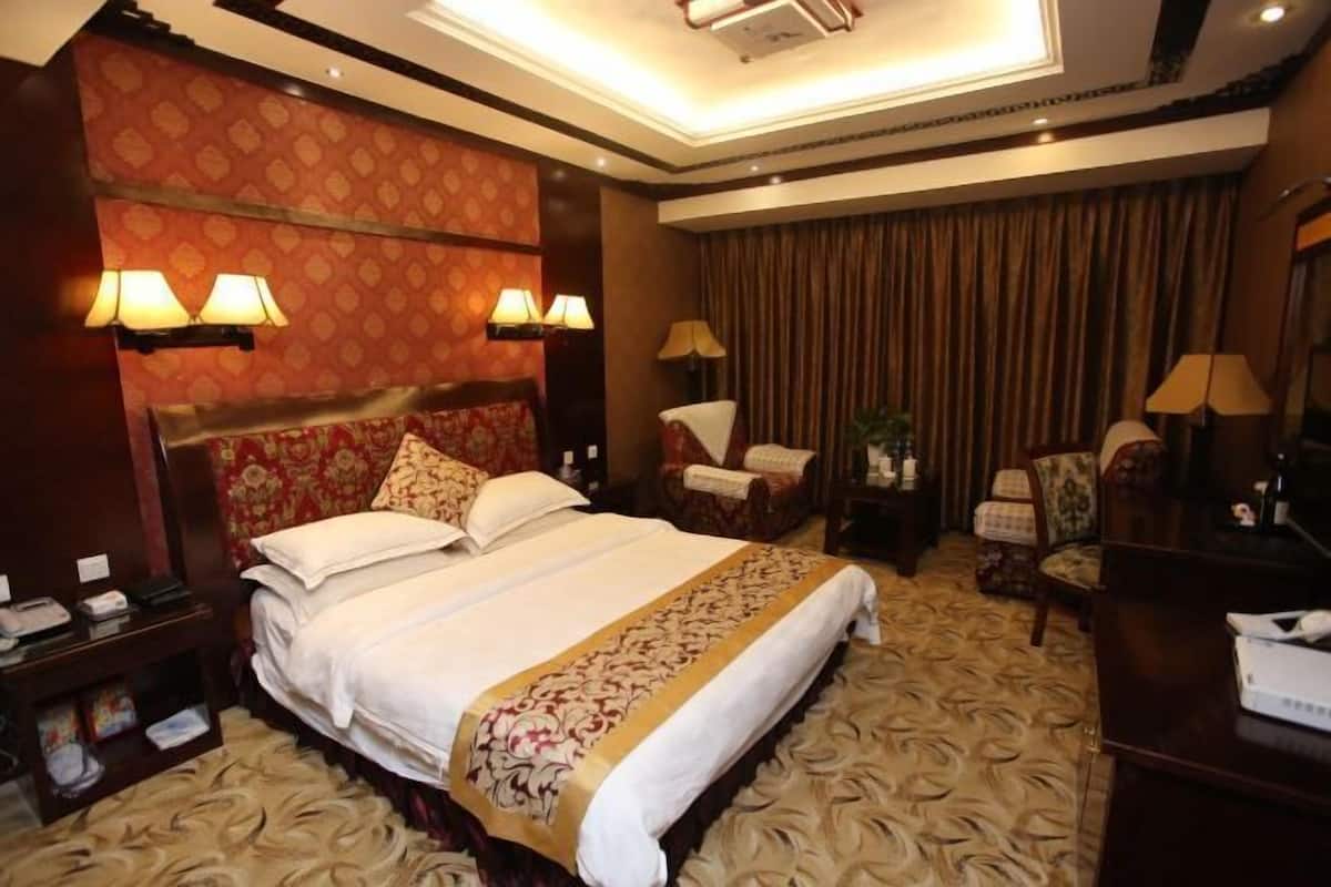 A hotel room with a large bed, two bedside lamps, a desk with a telephone, and a chair.