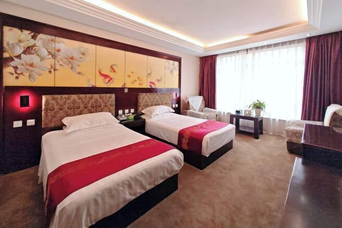 A hotel room with two beds, a desk, a chair, and a large window with curtains.
