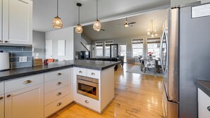Una cucina moderna con mobili bianchi, un'isola centrale, elettrodomestici in acciaio inossidabile, illuminazione a sospensione e un'area pranzo con vista.
