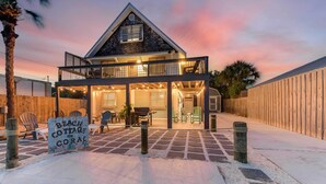 Ein zweistöckiges Strandhaus mit Balkon, einer überdachten Terrasse und einem Schild mit der Aufschrift 'Beach Cottage Coral'.
