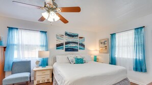 Ein Schlafzimmer mit Bett, Stuhl, Nachttisch, Deckenventilator und Bildern an der Wand.