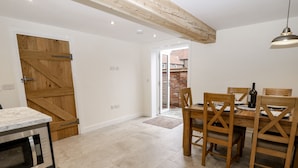 A modern kitchen with a built-in oven, a wooden door, and a dining area with a table and chairs. - The Grooms Cottage (York)