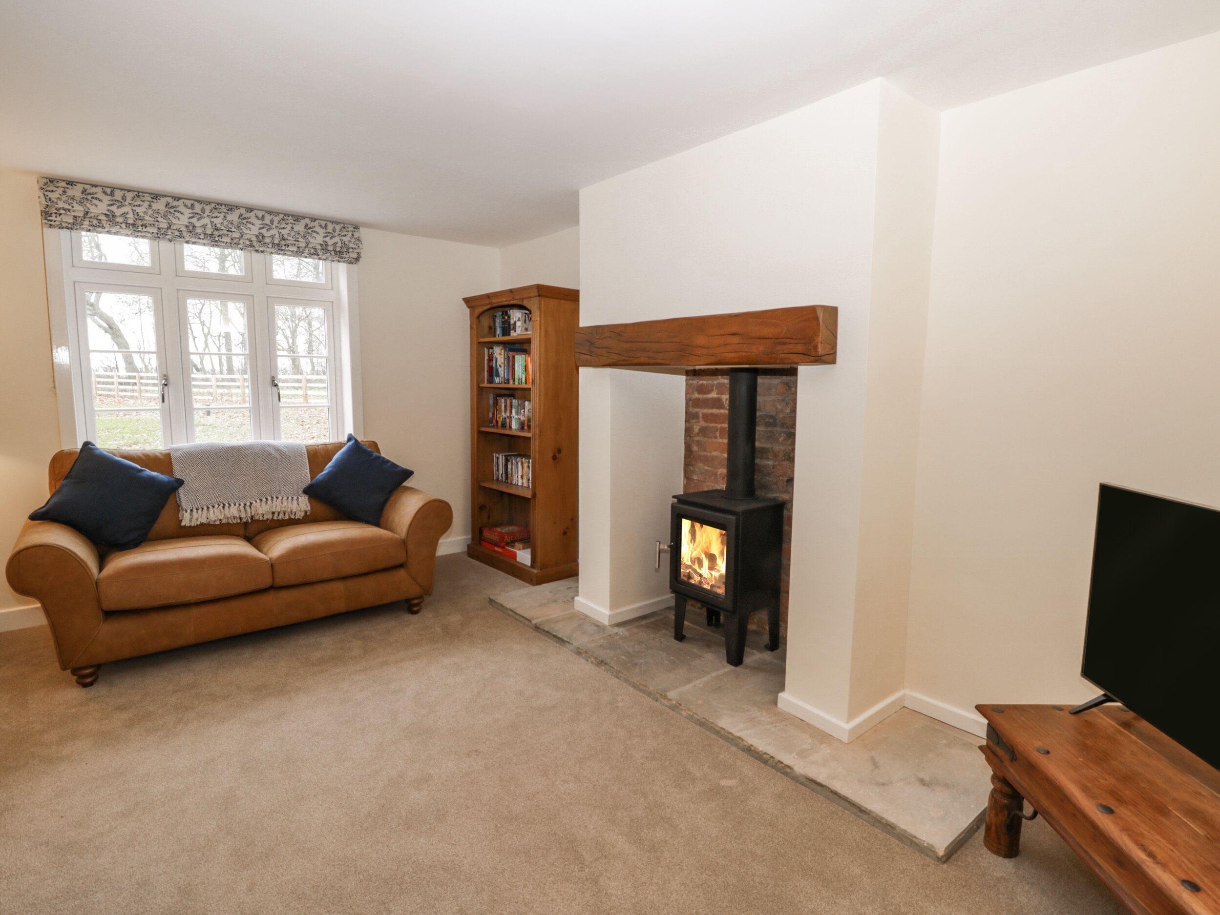 A living room with a brown leather sofa, a bookshelf, a fireplace, and a television.