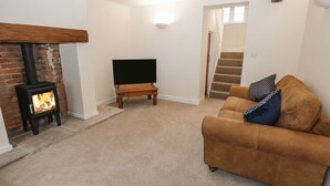 A cozy living room with a fireplace, a sofa, a TV, and a staircase. - The Grooms Cottage (York)