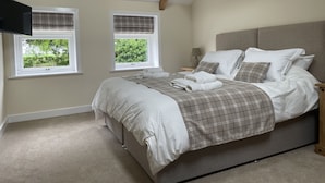 A bedroom with a bed, two windows, a television, and a nightstand with a lamp. - The Grooms Cottage (York)