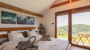 Een slaapkamer met een groot bed, een houten hoofdbord en uitzicht op een weelderig landschap door een glazen schuifdeur.