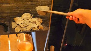 Iemand zit bij een open haard met een drankje, een houten schaal en een stenen pot.