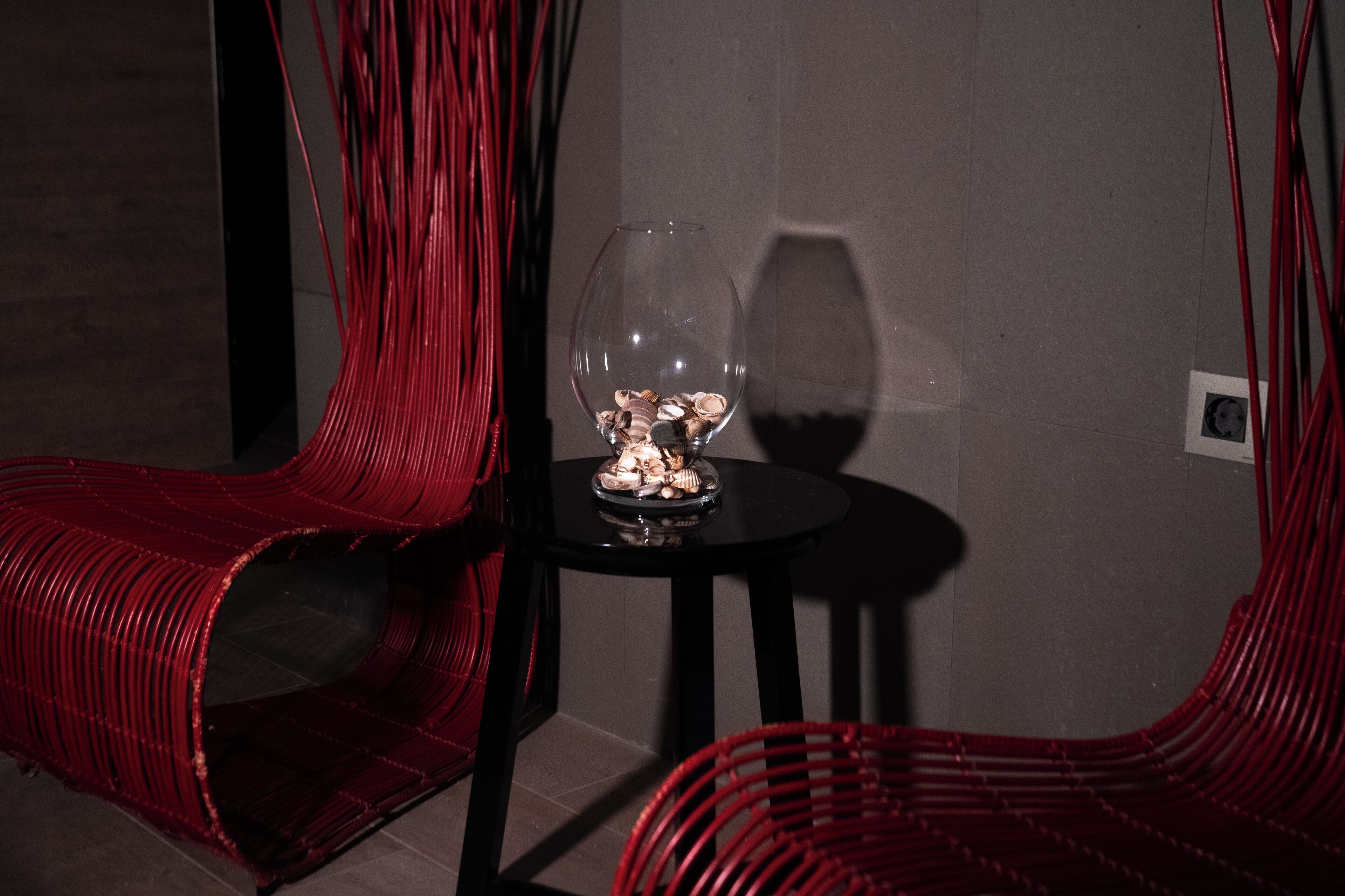 Une pièce avec une chaise rouge, une petite table ornée d’un objet décoratif et un mur avec un interrupteur.