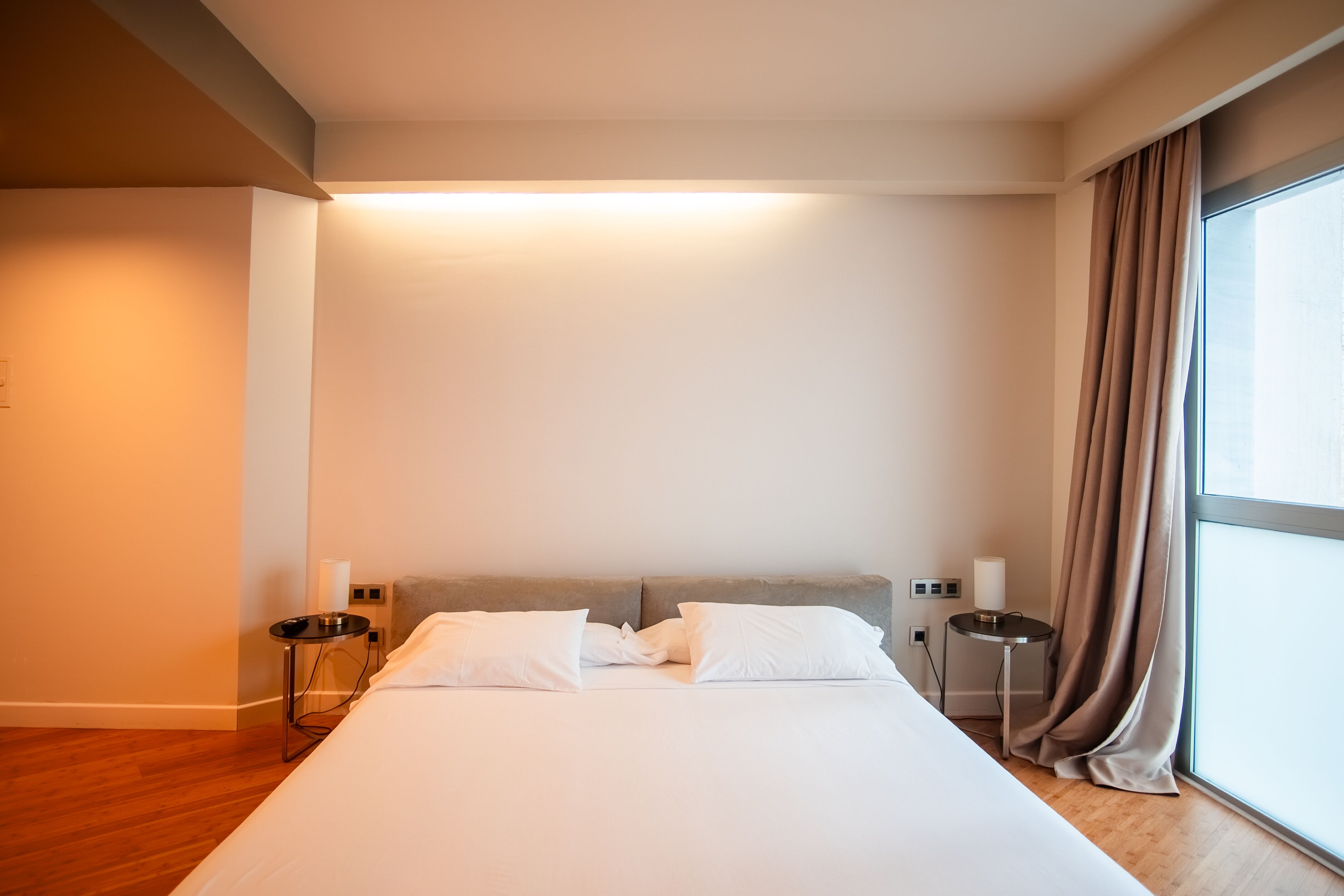 A modern hotel room with a large bed, a bedside table, a nightstand, and a window with curtains.