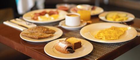 A breakfast table with plates of food, including toast, eggs, and a rolled pastry.