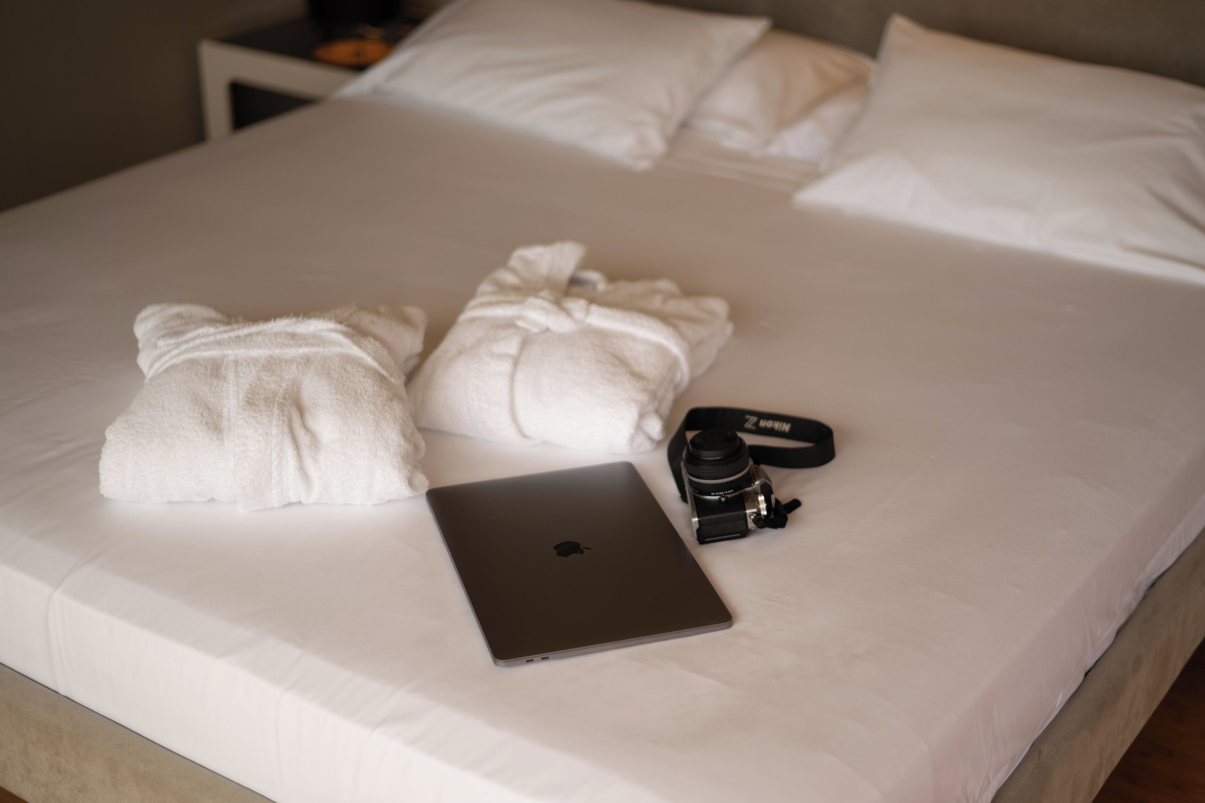 A neatly made bed with two white towels, a laptop, and a camera on it.