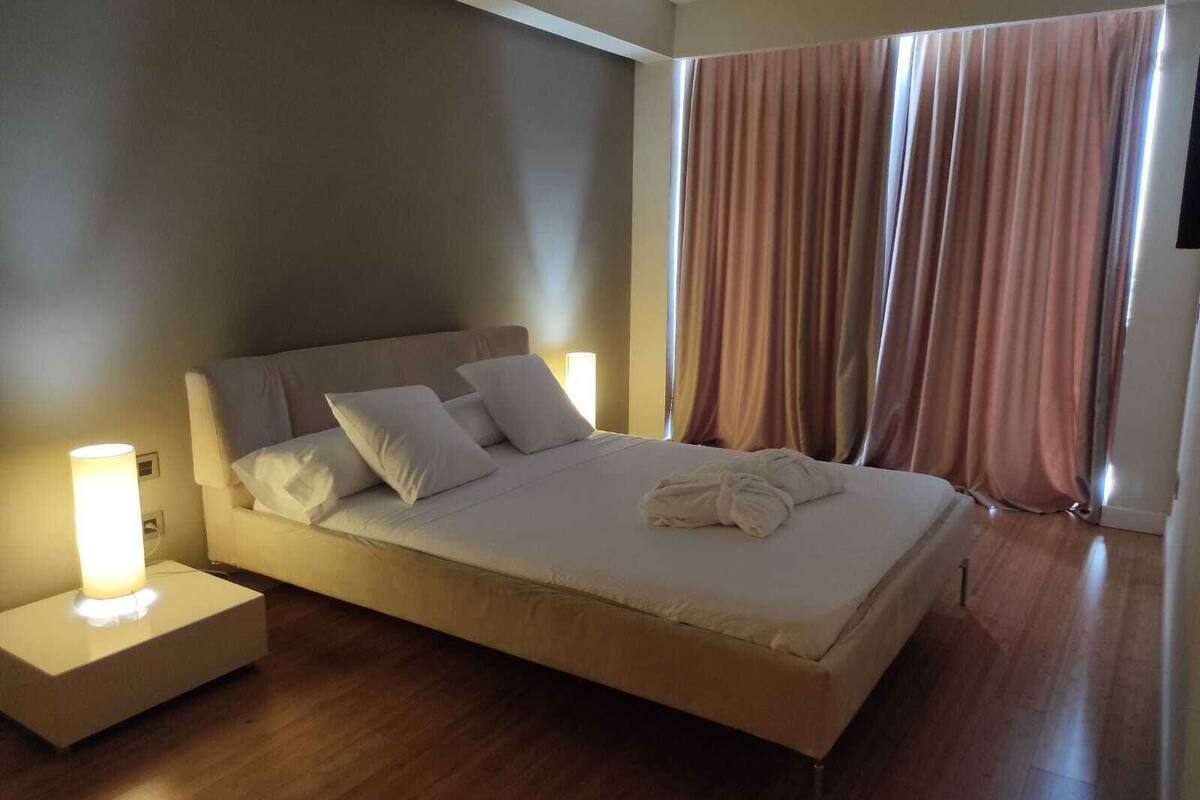 A neatly made bed with pillows and a towel, a bedside lamp, and a window with curtains.