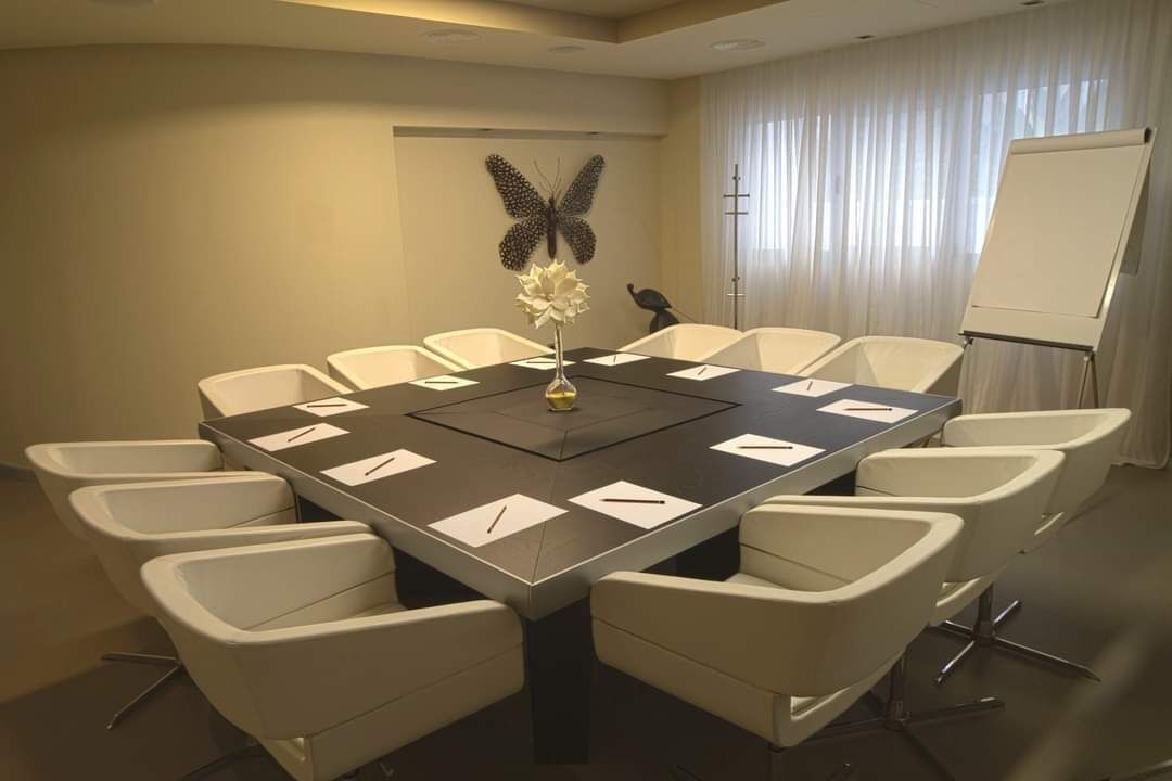 Un salón de conferencias con una gran mesa, sillas blancas, una pizarra y un adorno de mariposa en la pared.
