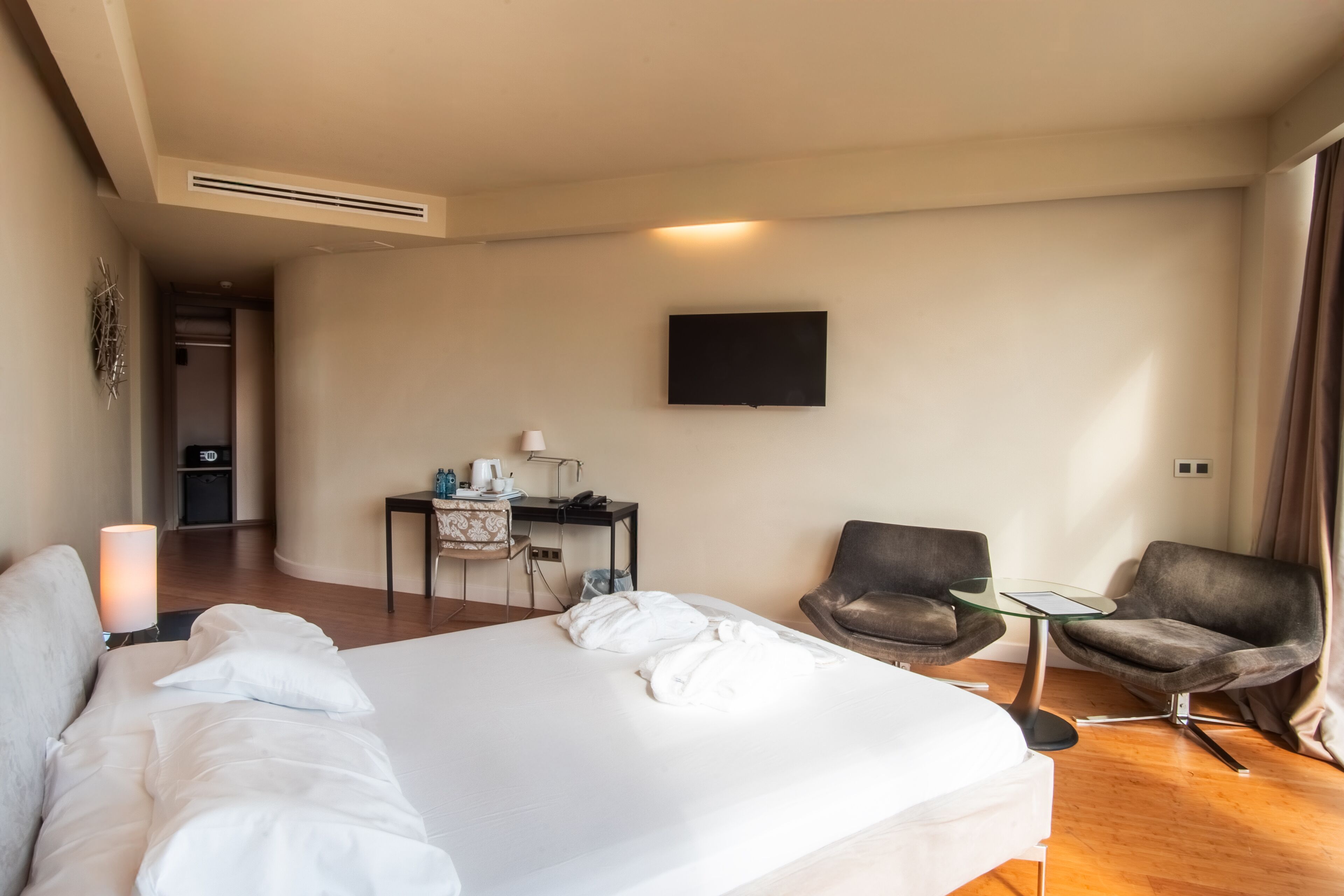 Una camera d'hotel con un letto grande, una scrivania con una sedia, un televisore fissato alla parete e un tavolino con due sedie.