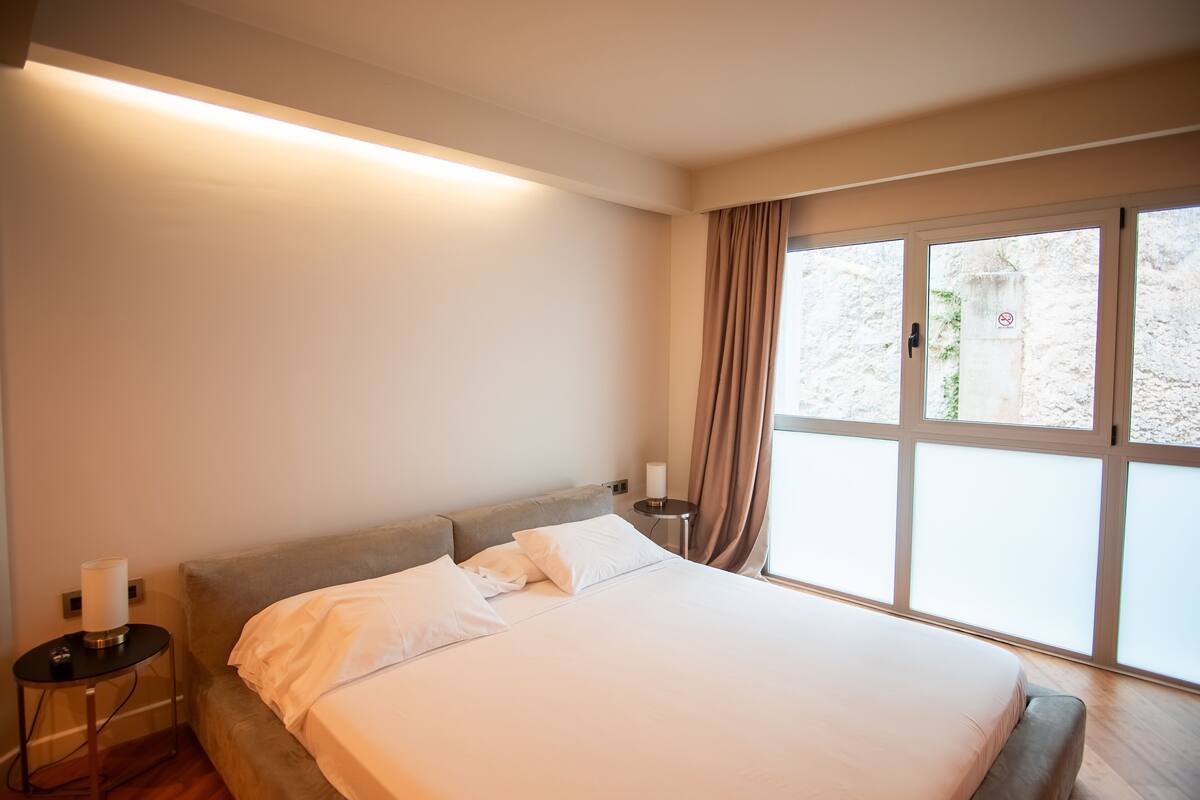 A hotel room with a large bed, a bedside table, a lamp, and a window with curtains.