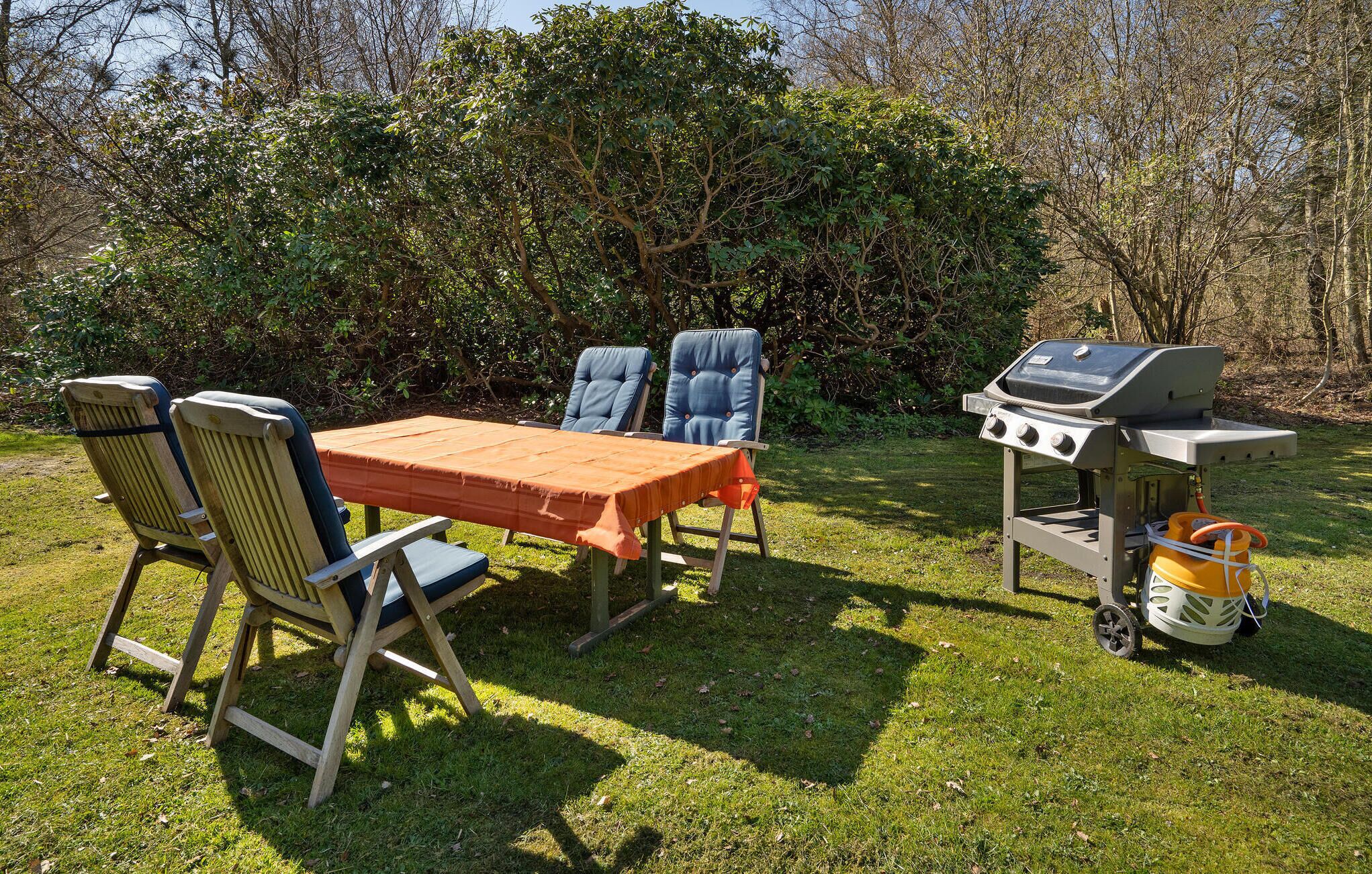 Un espacio de comedor al aire libre con una mesa, sillas, una parrilla y un tanque de gas.