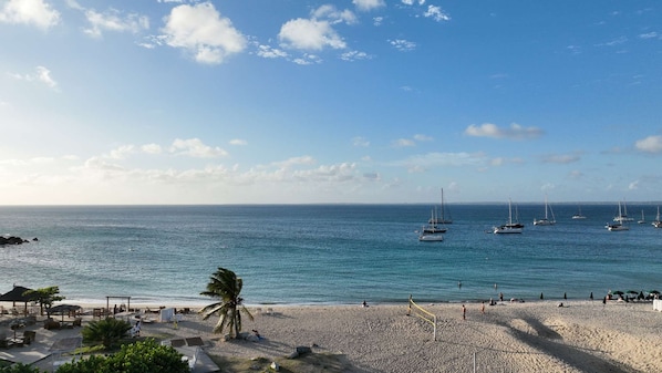 Una playa con vista despejada al océano, varios veleros y una orilla arenosa con sombrillas y sillas de playa.