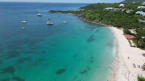 Eine Küstenregion mit sandigem Strand, klarem türkisblauem Wasser und mehreren vor der Küste vor Anker liegenden Booten.