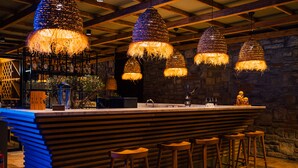 A bar area with a wooden bar counter, multiple hanging light fixtures, and bar stools.