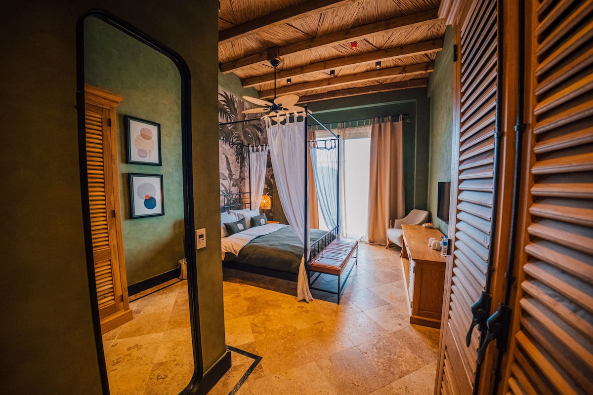A bedroom with a bed, a desk, a chair, a ceiling fan, and a window with curtains.