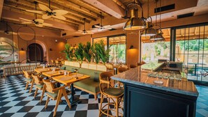 A restaurant with checkered flooring, wooden tables and chairs, a bar area, and large windows offering a view of greenery.