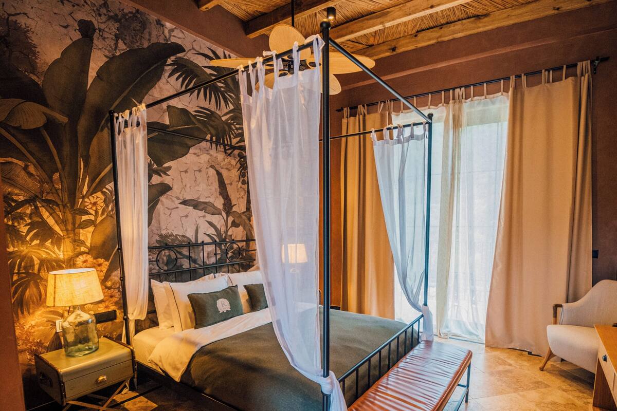 A room with a four-poster bed, a bench, a nightstand, and a lamp.