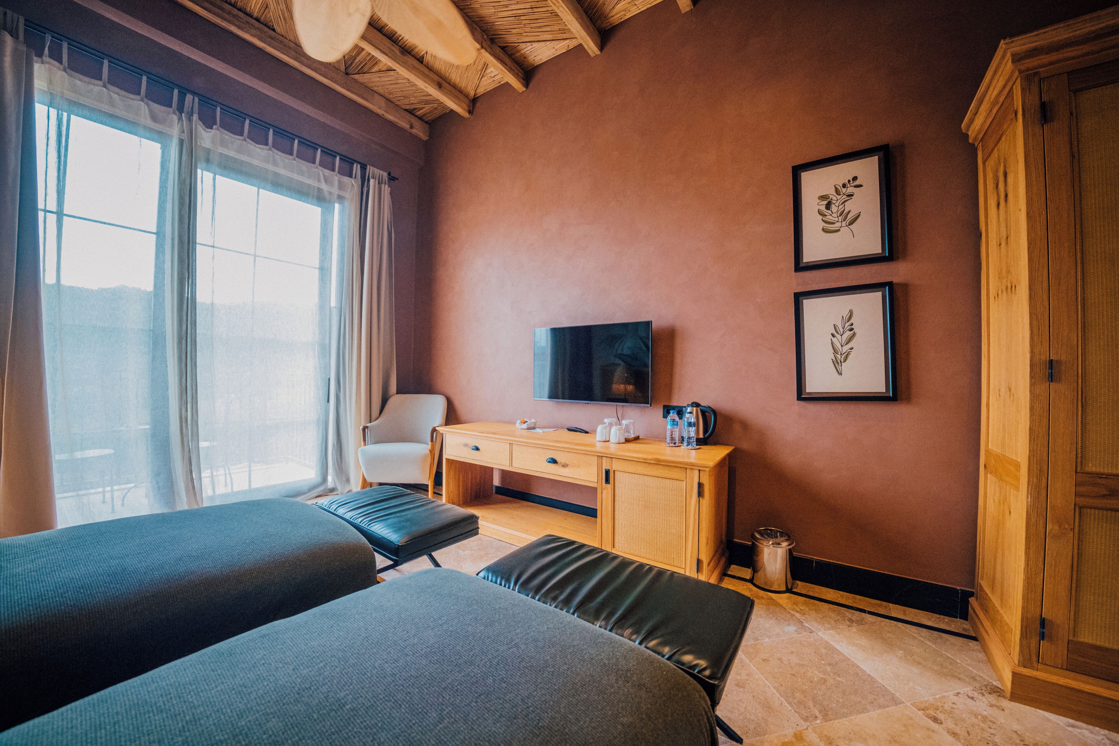 A hotel room with two beds, a desk with a TV, and framed pictures on the wall.