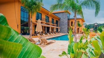 A modern house with a swimming pool, lounge chairs, and tropical plants.