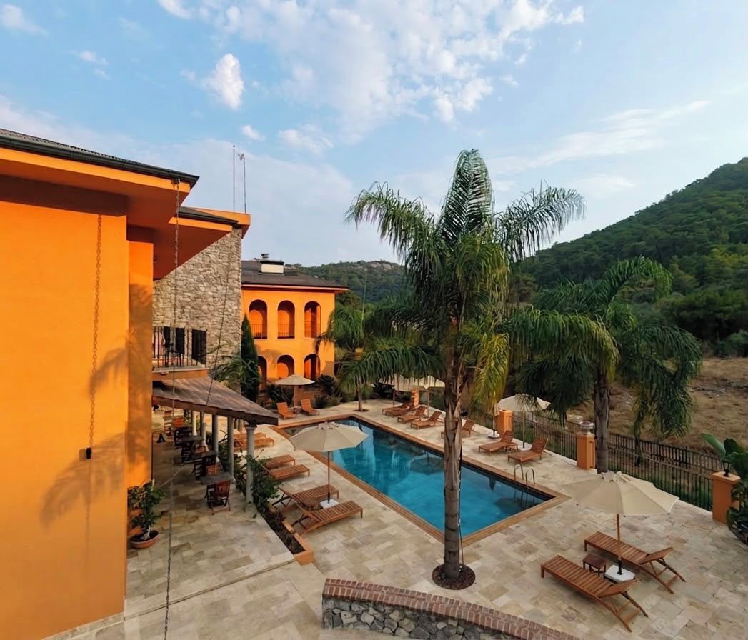 A pool area with lounge chairs and a palm tree, surrounded by a building with arches and a stone facade.