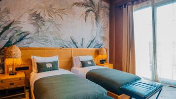Habitación de hotel con dos camas, un mural grande de palmeras, un ventilador de techo y vistas al exterior a través de una ventana.