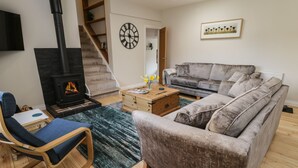 Ein Wohnzimmer mit Kamin, einer Couch, einem Sessel, einem Couchtisch und einer Treppe.