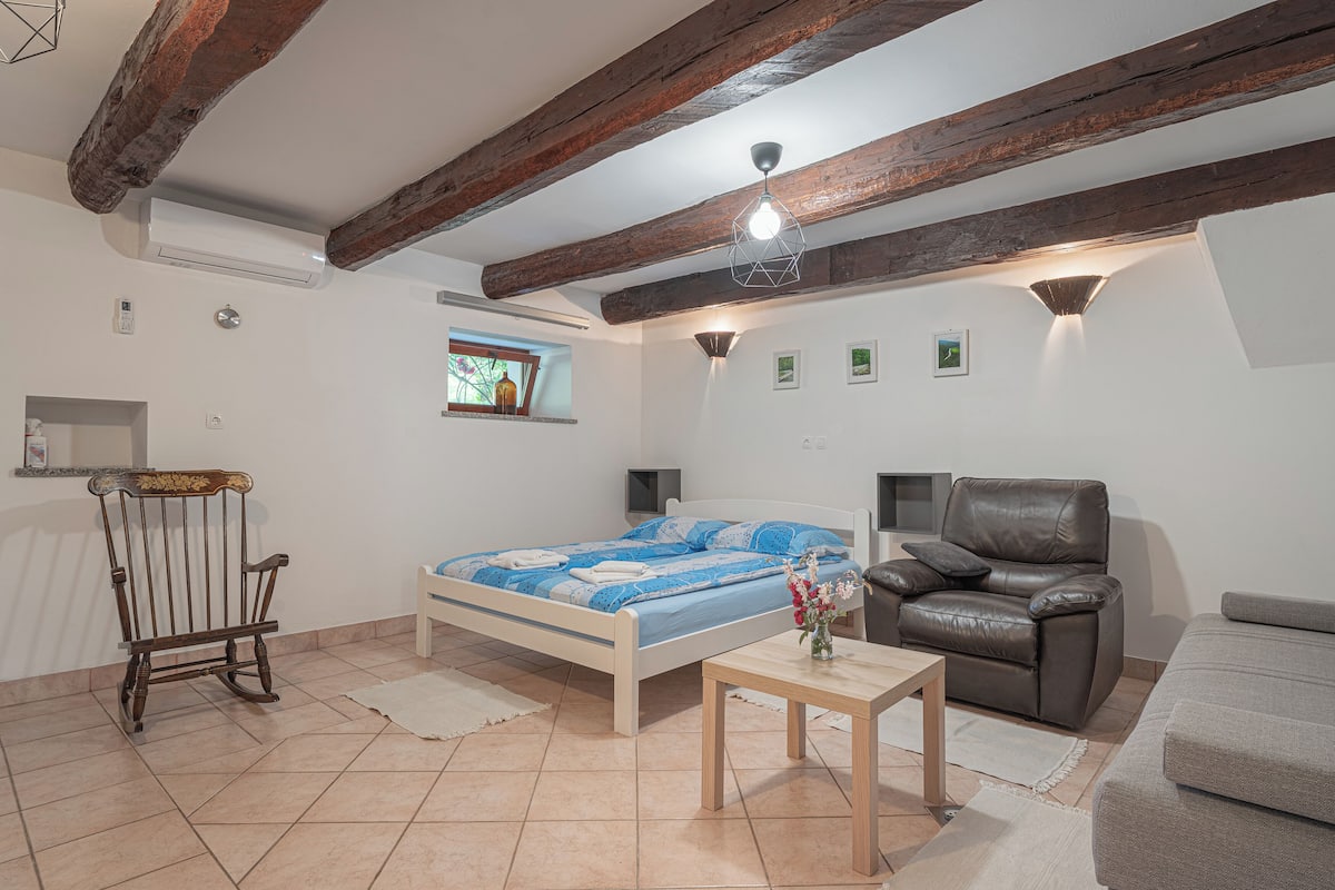Une chambre à coucher comprenant un lit, un fauteuil à bascule en bois, un fauteuil en cuir, une petite table et un canapé.