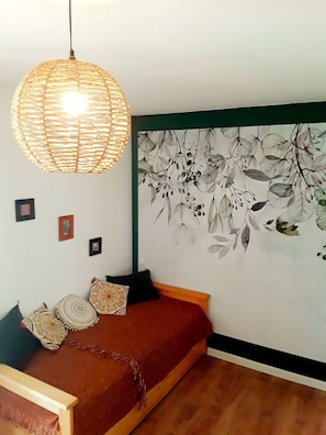 Une chambre avec un lit, un luminaire suspendu en fibres tressées, une fresque murale et un plancher en bois.