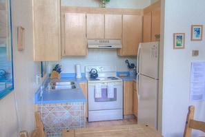 Eine kleine Küche mit Holzschränken, einer Edelstahl-Spüle, einem weißen Herd und einem Kühlschrank.