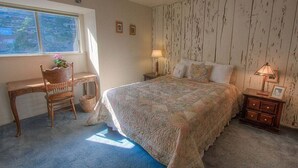 Ein Schlafzimmer mit einem großen Bett, einem Holztisch, einem Stuhl, einem Nachttisch mit Lampe und einem Fenster mit Jalousien.