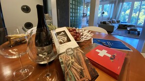 A dining table with a wine bottle, wine glasses, a bowl of grapes, and a book titled "Fine Food". - Luxury loft downtown Geneva (Geneva)