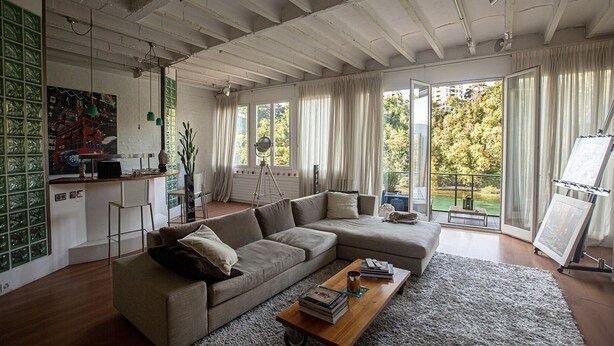 A modern living room with a sectional sofa, a coffee table, and a balcony with a view of trees. - Luxury loft downtown Geneva (Geneva)