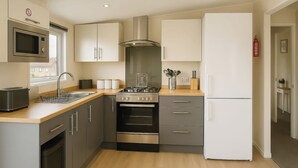 A modern kitchen with a stainless steel range, a built-in oven, a microwave, and a white refrigerator. - Birch Lodge (Carnforth)