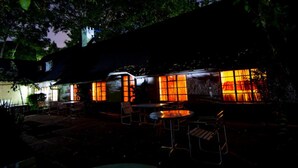 Un espace extérieur aménagé en terrasse, avec des tables et des chaises, une petite piscine et un bâtiment dont les fenêtres sont illuminées.