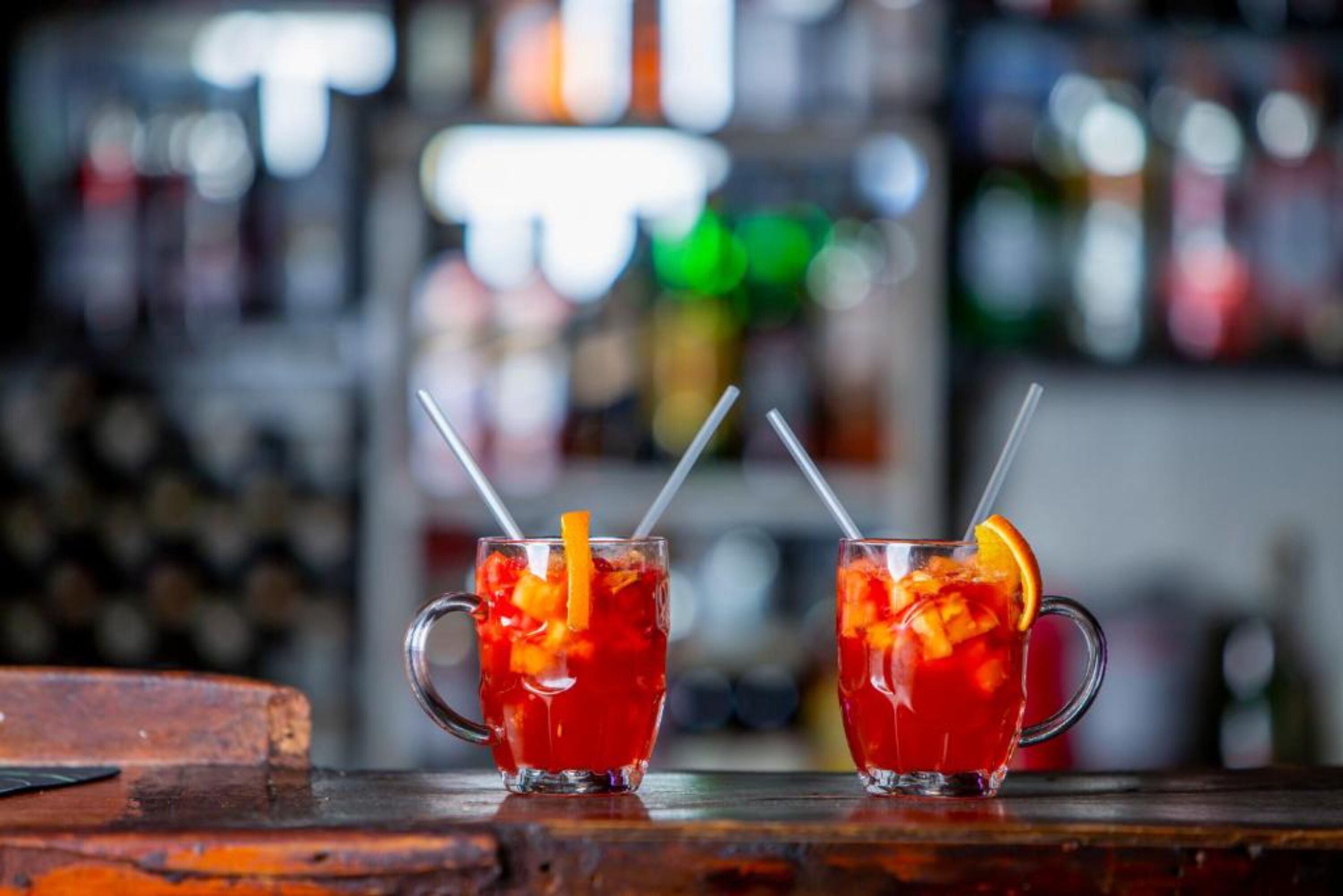 Two glasses of red beverage with straws and orange slices on a wooden bar counter.