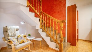 Sala de estar con sofá, una mesita, una planta en maceta y una escalera con pared roja.