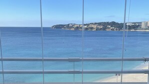 Quarto com uma grande janela com vista para uma praia e um litoral distante.