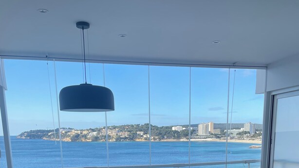 Uma sala de estar moderna com uma janela ampla que oferece vista para a costa, uma mesa de jantar redonda com cadeiras, um sofá e uma tigela decorativa.