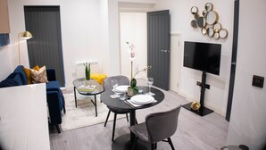 A modern living room with a sofa, a dining table set with plates and glasses, a TV, and a decorative mirror wall.