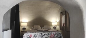 A bedroom with a curved ceiling, two bedside lamps, a floral bedspread, and a nightstand with a vase.