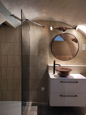 Ein modernes Badezimmer mit Duschkabine aus Glas, einem runden Spiegel und einem Waschbecken aus Holz.