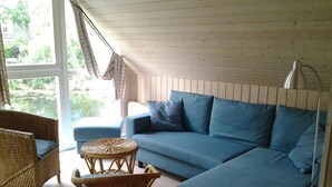 Ein gemütliches Zimmer mit einem blauen Sofa, Korbstühlen und einem kleinen runden Tisch.
