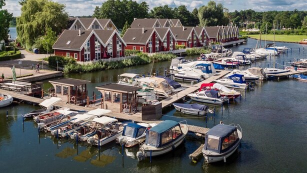 Ein Yachthafen mit vertäuten Booten, eine Reihe roter Häuser und ein ruhiger Fluss.